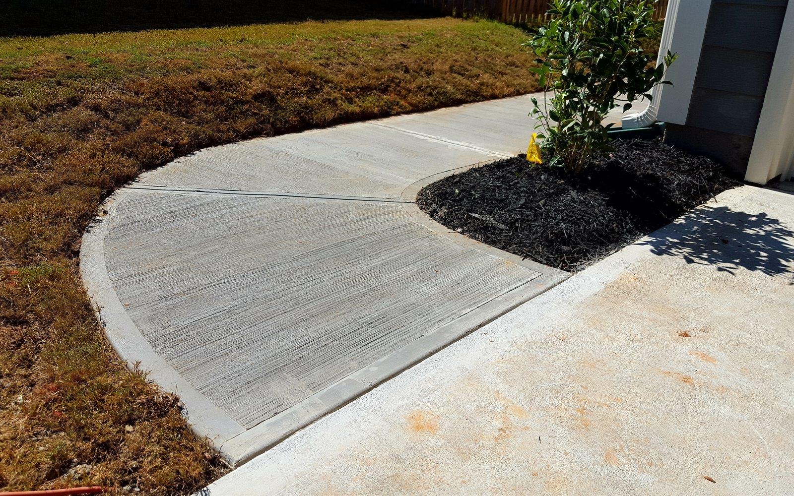 Curved broom-finish concrete walkway beside a fresh mulch bed