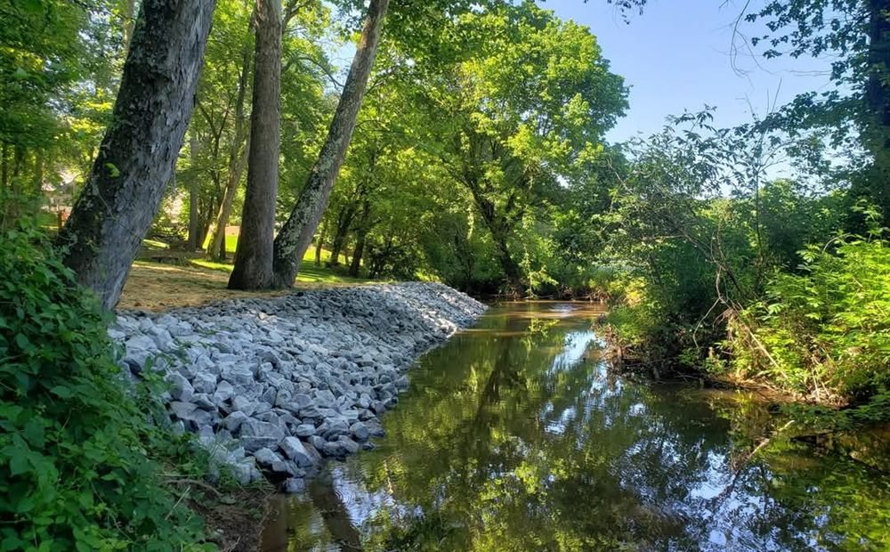 Rip-rap creek-bank stabilization along a clear stream under a green canopy