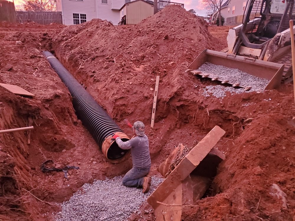 Crew installing a corrugated drain line in a red-clay trench