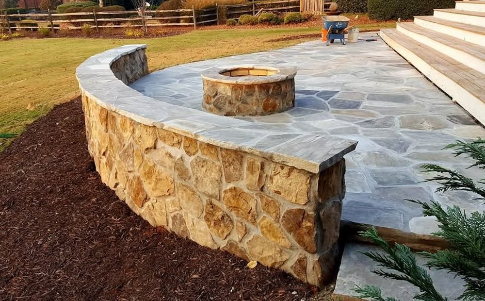 Curved stone seat wall with a built-in fire pit glowing at dusk