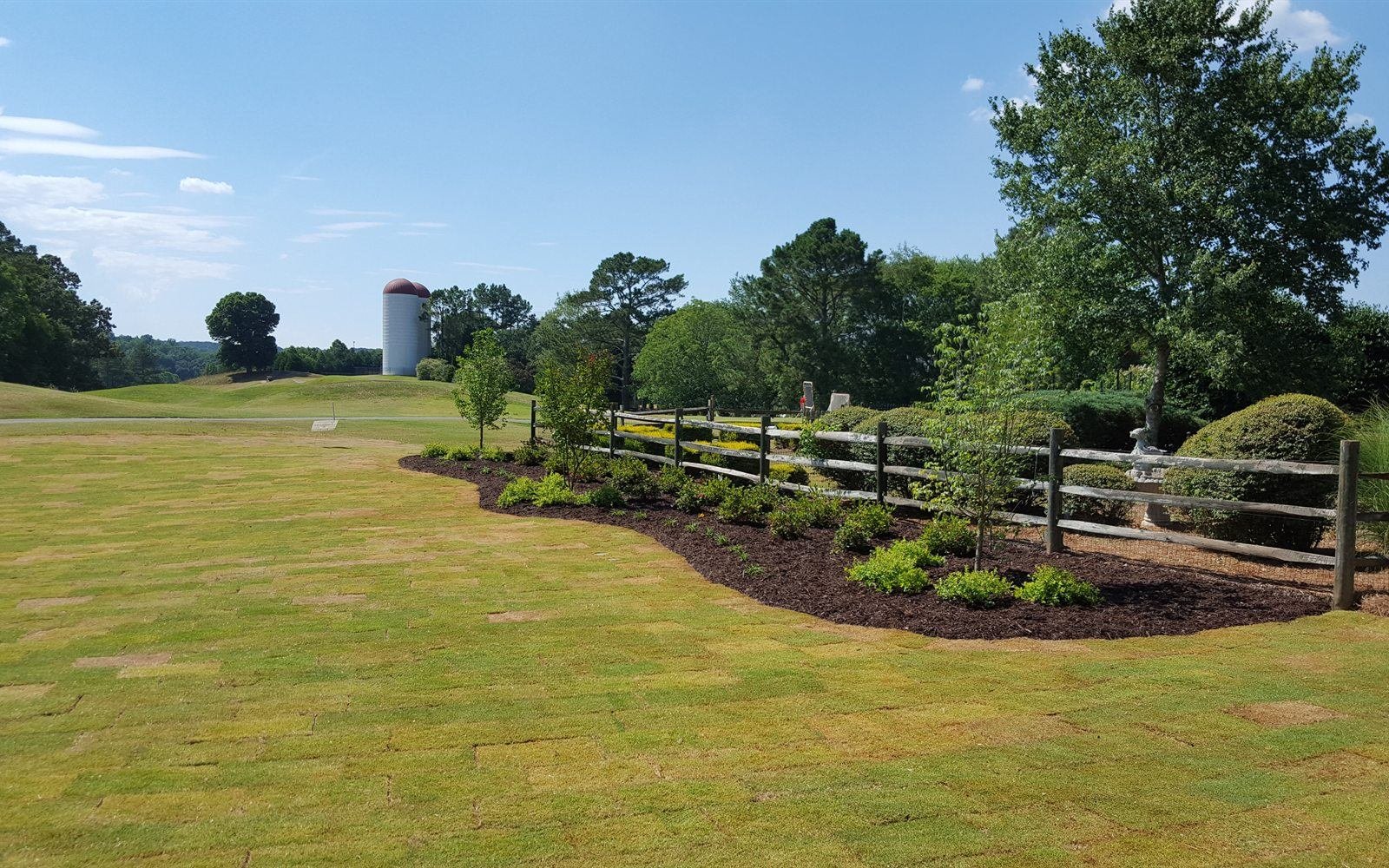 Sweeping estate lawn with a curved mulch bed and freshly planted trees in North Georgia
