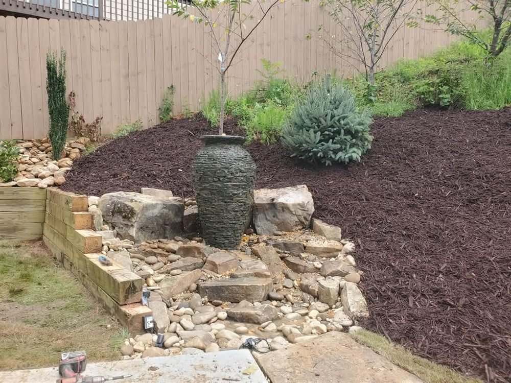 Stacked-stone bubbling urn water feature set in a boulder-edged planting bed