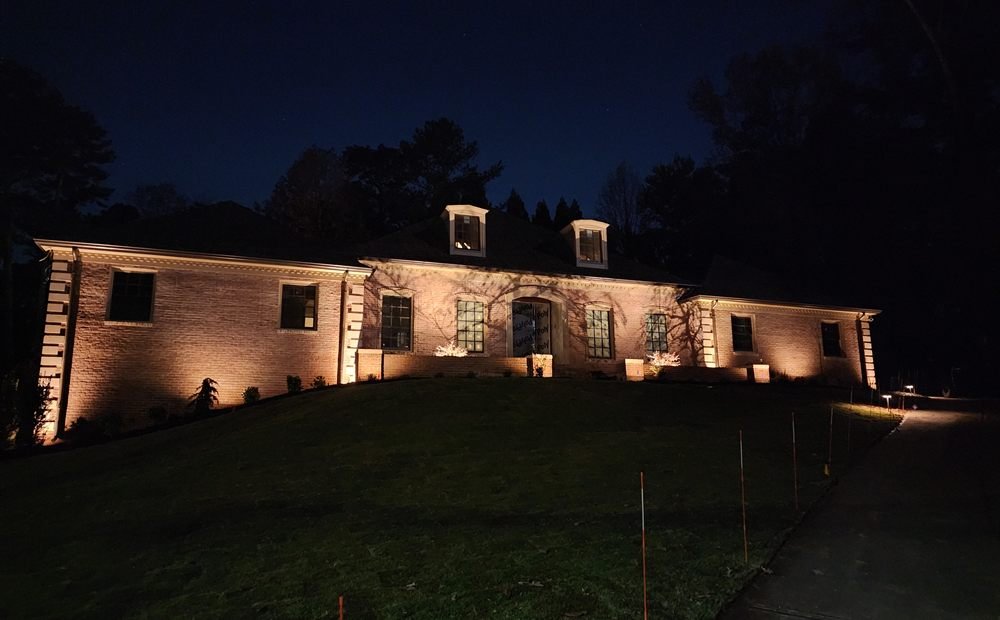 Warm landscape uplighting washing over a brick home facade at dusk