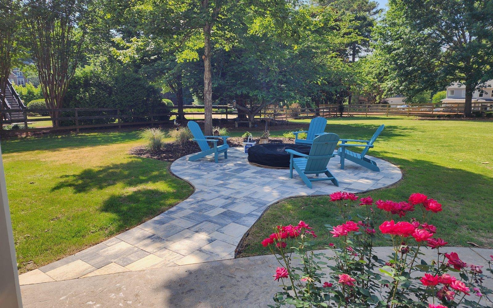 Paver firepit patio with Adirondack chairs, blooming roses and a manicured lawn