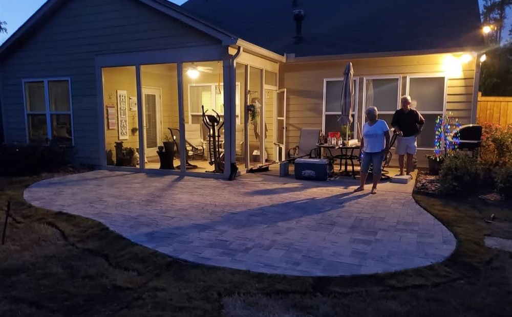 Curved paver patio lit softly at dusk behind a home