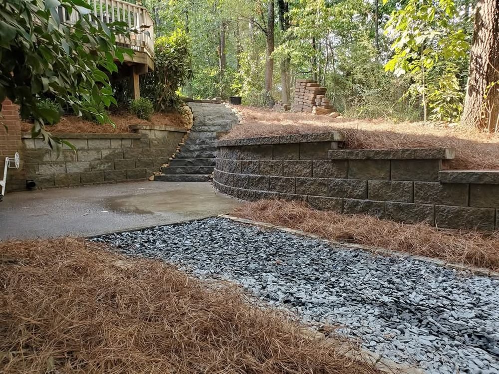 Modular block retaining wall with a cobble drainage swale on a wooded lot