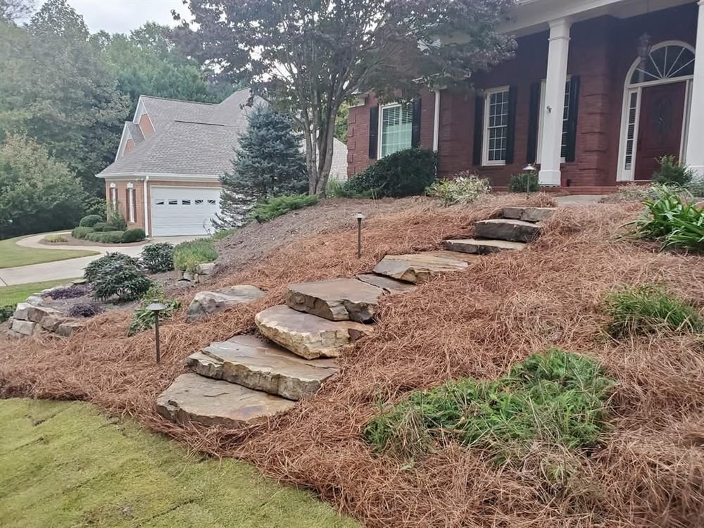 Natural fieldstone boulder steps climbing a pine-straw slope to a brick home